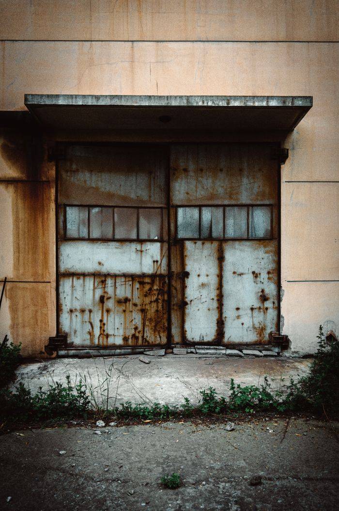 A weathered, rusty metal door in an abandoned urban setting, perfect for backgrounds and textures.